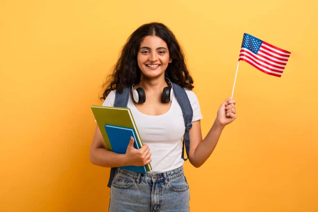 Young woman holding US flag and textbooks, representing Indian students in America.