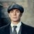 Man wearing a flat cap, suit, and tie with a serious expression.